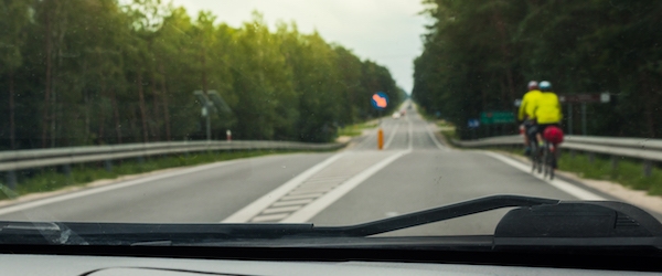 A view through the front windshield of a car, with two bicyclists on the road ahead.